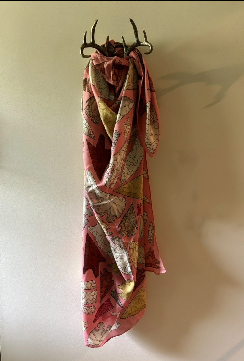 A pink scarf with a vintage map print hangs from a decorative antler coat rack against a plain beige wall.